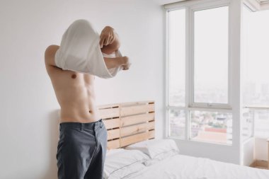 Adam yatak odasında tişörtünü çıkarıyor..