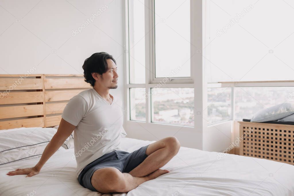 Happy man sits and relax on his bed in his apartment.