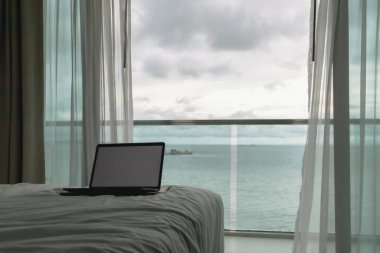 Çalışma konsepti. Yatak ve okyanus manzaralı balkonda boş ekran laptop.