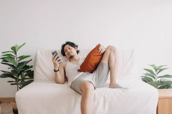 Sıkılmış adam rahatlamış ve akıllı telefonu evde yalnız zaman geçirmek için kullanmış.. — Stok fotoğraf