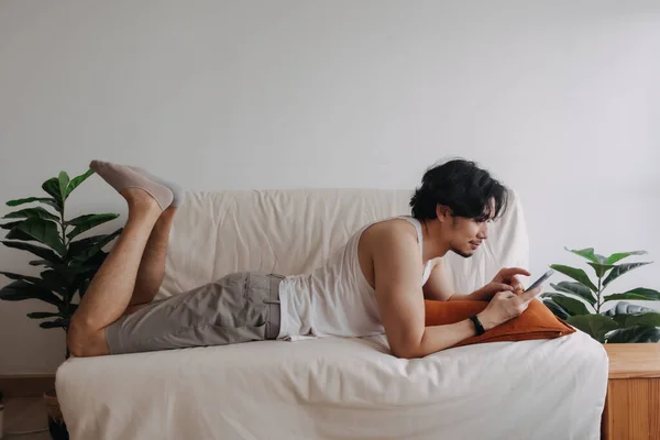 Pria bosan santai dan menggunakan smartphone untuk membunuh waktu sendirian di apartemen. — Stok Foto