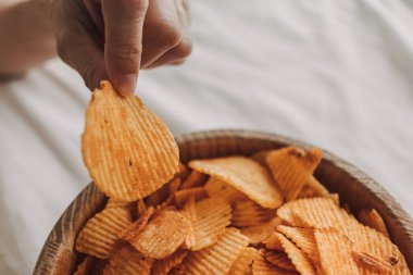 Beyaz yatakta bir kase patates cipsi..