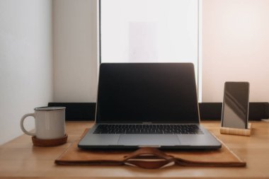 Dizüstü bilgisayar çalışma alanı pencerelerin yanındaki ahşap masada..