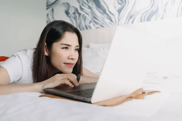 Woman works with laptop on the bed in concept of workation.