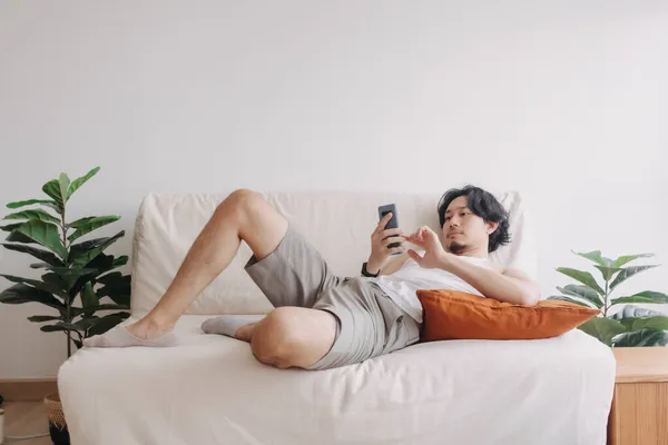 Поганий чоловік розслаблений і використовує смартфон для вбивства часу наодинці в квартирі . — стокове фото