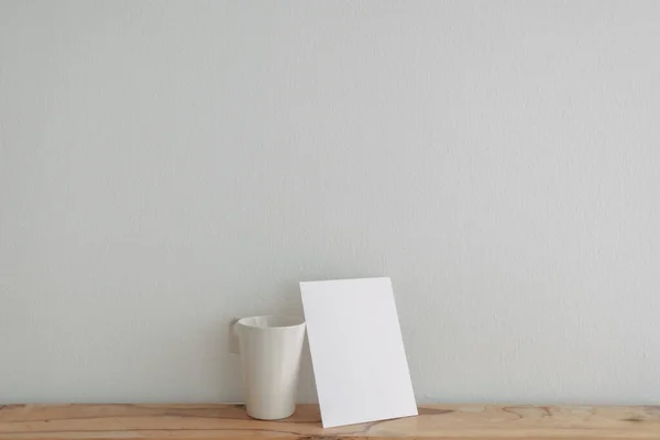 Пустая белая карточка макет опирается на чашку чая с белой стеной. — стоковое фото