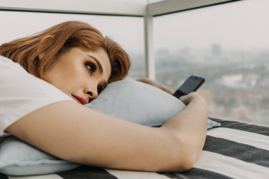 Kadın dinleniyor ve elinde akıllı telefonuyla odada dinleniyor..