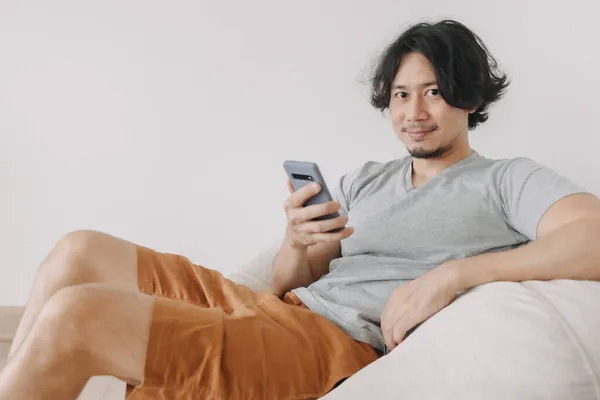 Mann benutzt Smartphone beim Sitzen und Entspannen auf Sofa. — Stockfoto