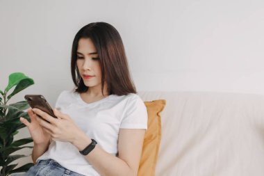 Kadın apartmandaki oturma odasında akıllı telefon kullanıyor..