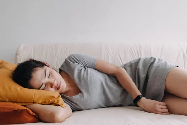 Femme en robe grise dort et se détend sur le canapé de l'appartement. — Photo