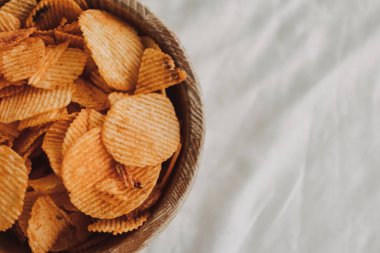 Beyaz çarşaf üzerinde bir kase patates cipsi..