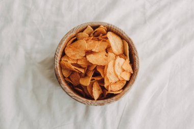 Beyaz yatakta bir kase patates cipsi..