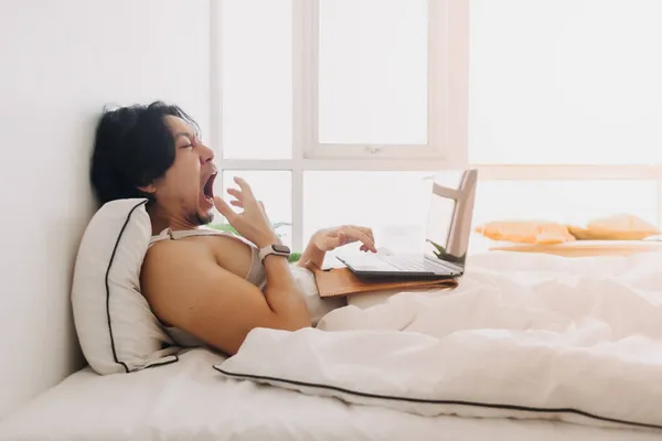El hombre se despierta y trabaja con el ordenador portátil en la cama a primera hora de la mañana. — Foto de Stock