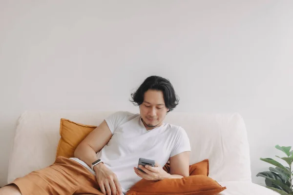 Freelance pria rambut panjang duduk di sofa dan menggunakan aplikasi smartphone. — Stok Foto