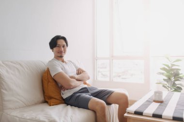 Mutlu adam dairenin oturma odasındaki kanepede oturur ve dinlenir..