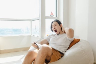 Adam rahatlar ve evinde kanepede kitap okur..