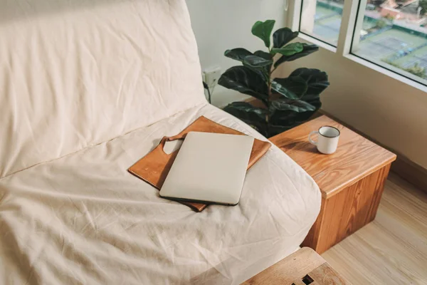 Laptop met leren mouw op beige bank in de woonkamer. — Stockfoto