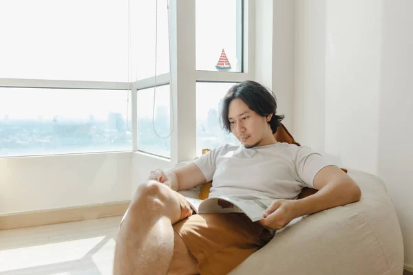 Man santai dan membaca buku di sofa kantong kacang di apartemennya. — Stok Foto