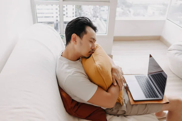 El hombre trabaja desde casa con su portátil en el apartamento, pero cansado y dormido. — Foto de Stock