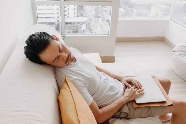 El hombre trabaja desde casa con su portátil en el apartamento, pero cansado y dormido. — Foto de Stock