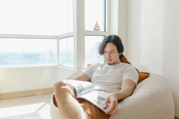 Hombre relajarse y leer libro en el sofá de la bolsa de frijoles en su apartamento. — Foto de Stock