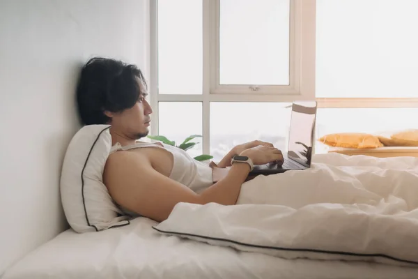 Чоловік прокидається і працює з ноутбуком на ліжку перше вранці . — стокове фото