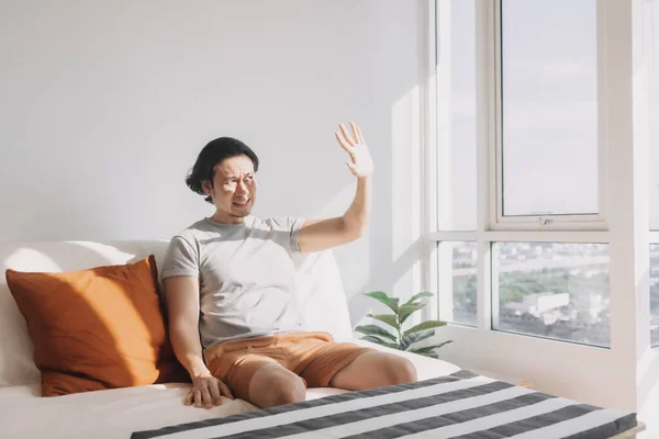 El hombre usa su mano para cubrir la luz del sol caliente que brilla en su sala de estar. —  Fotos de Stock