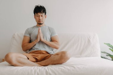 Asyalı adam evinde kanepede meditasyon yapıyor..