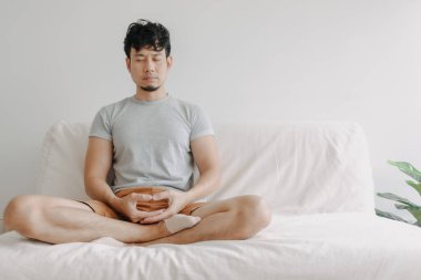 Asyalı adam evinde kanepede meditasyon yapıyor..