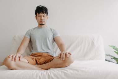 Asyalı adam evinde kanepede meditasyon yapıyor..