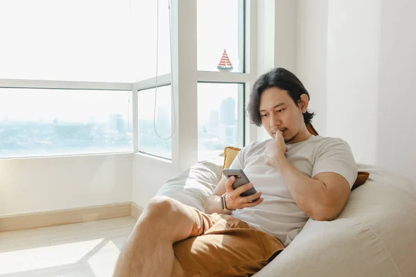 Man menggunakan smartphone sementara duduk dan bersantai di sofa kantong kacang di apartemennya. — Stok Foto