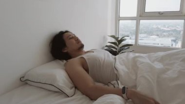 Bir adam uyanıyor beyaz yatağında, yatak odasının dairesinde, rahat, tembel bir sabah.