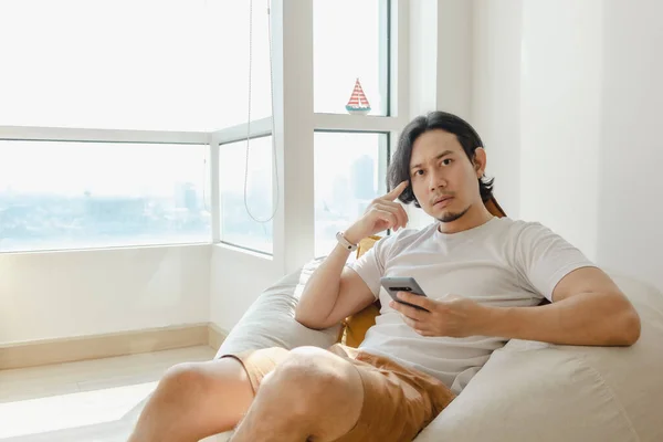 Homem usar smartphone enquanto se sentar e relaxar no sofá saco de feijão em seu apartamento. — Fotografia de Stock