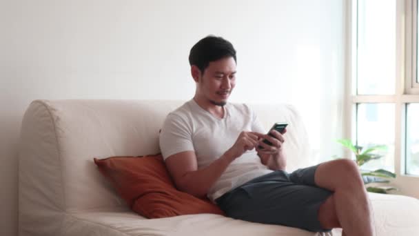 Glücklicher Mann benutzt sein Handy im Wohnzimmer an einem lockeren Tag. — Stockvideo