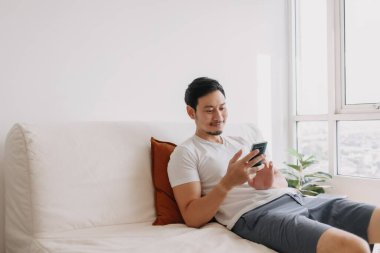 Happy man using smartphone in his living room in a casual day.