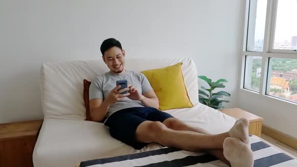 男は彼のソファでリラックスしながら、モバイルアプリケーションに満足. — ストック動画