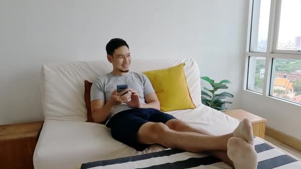Asian Man Happy Mobile Application While Relax His Sofa — Stock Video