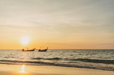 Phuket Thailand 'daki Mai Khao Sahili' nin gün batımı manzarası ve iki uzun kuyruk teknesi..