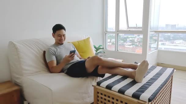 Asijský Muž Při Pohledu Jeho Mobil Zatímco Relaxovat Pohovce Svém — Stock video
