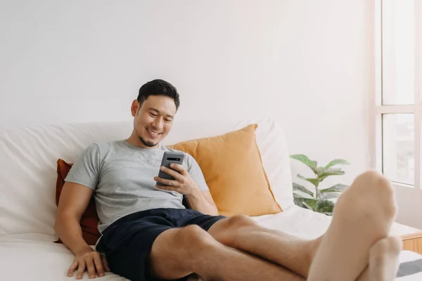 Asian man happy with the mobile application while relax on his sofa.