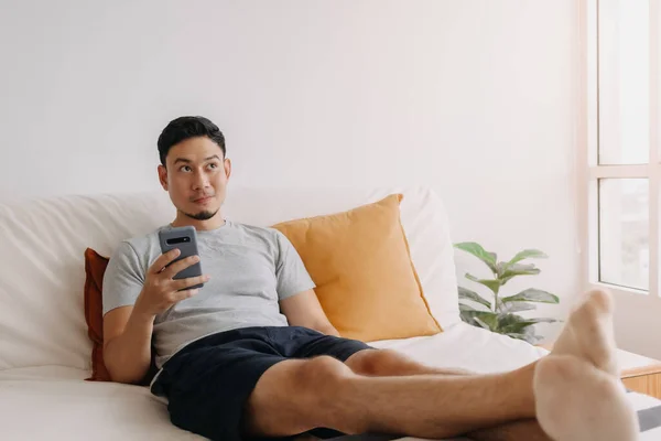 Asian man happy with the mobile application while relax on his sofa.