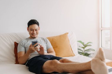 Kanepesinde dinlenirken Asyalı adam mobil uygulamadan memnun..