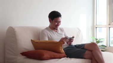 Asyalı adam akıllı telefondaki oyuna odaklanır ve konsantre olur..