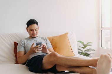 Kanepesinde dinlenirken Asyalı adam mobil uygulamadan memnun..