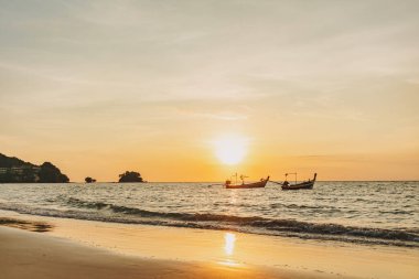 Phuket Thailand 'daki Mai Khao Sahili' nin gün batımı manzarası ve iki uzun kuyruk teknesi..