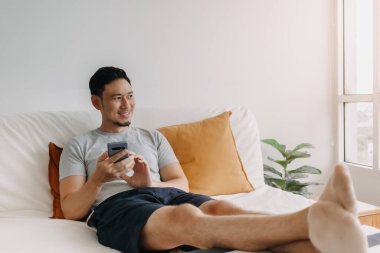 Asian man happy with the mobile application while relax on his sofa.