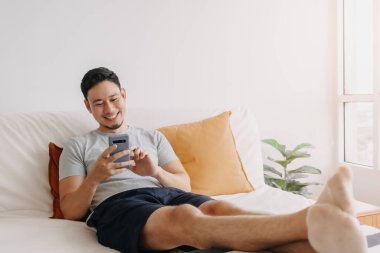 Asian man happy with the mobile application while relax on his sofa.