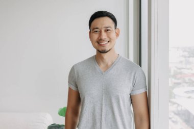 Ordinary happy life smile face asian man stand by the window in his apartment.