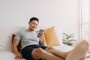 Asian man happy with the mobile application while relax on his sofa.