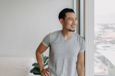 Ordinary happy life smile face asian man stand by the window in his apartment.
